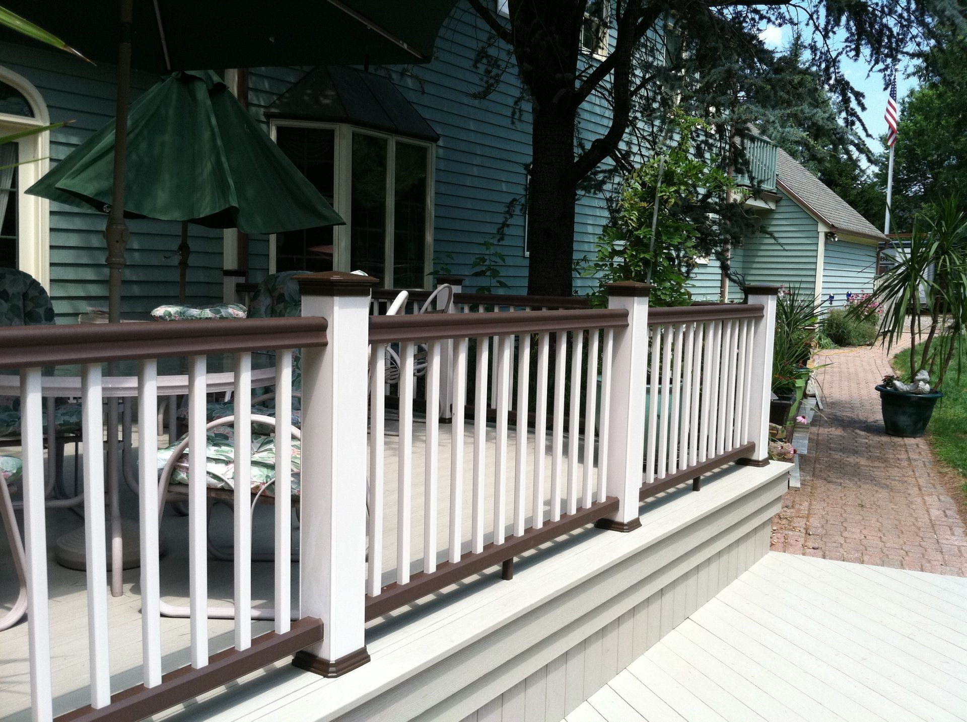 Close-up of brown and white deck railing with outdoor seating and green umbrellas.