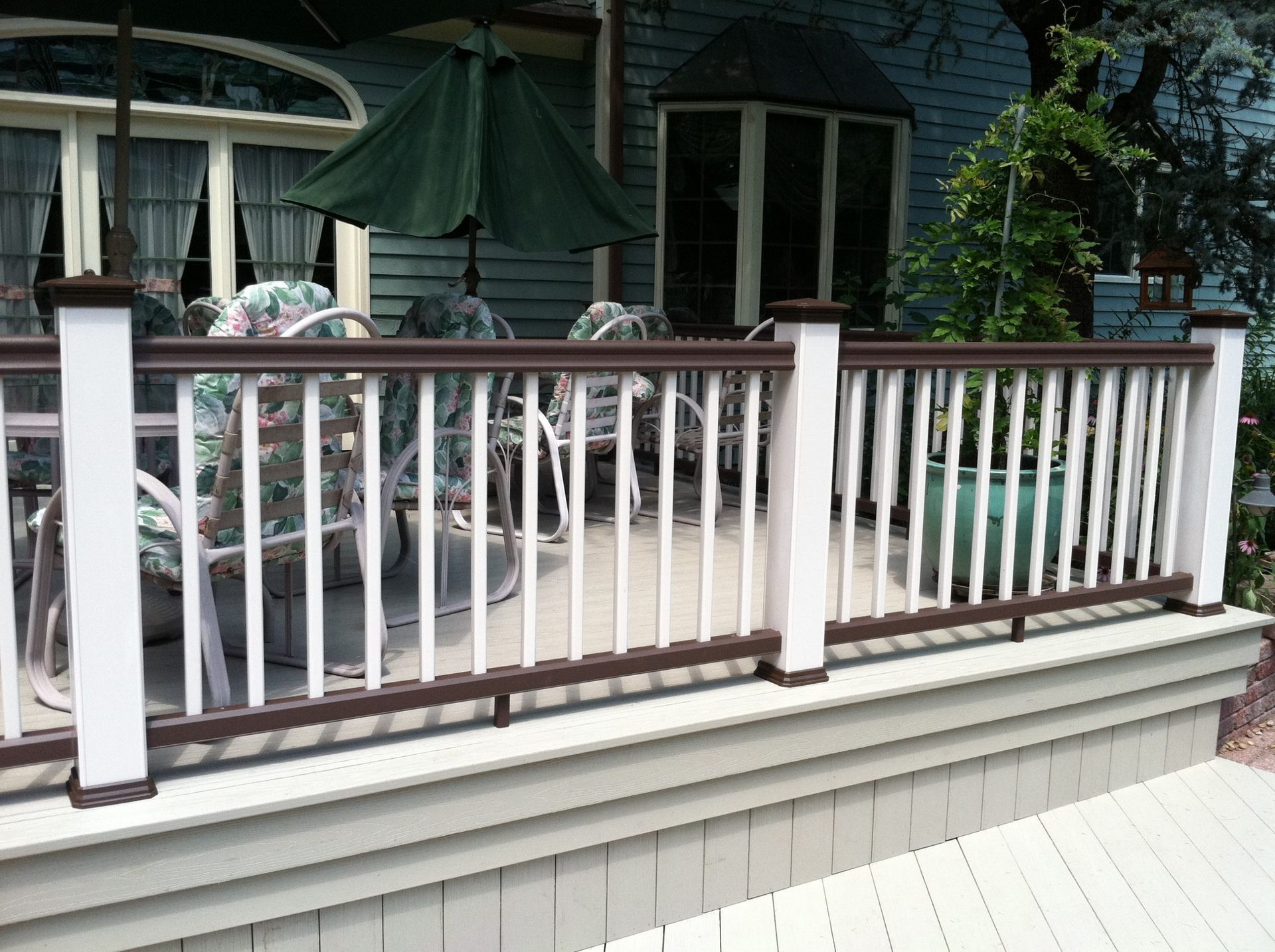 Deck railing featuring brown top rail and white balusters overlooking outdoor seating area.