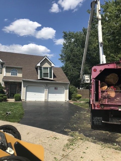 Truck with a pink recycling dumpster beside a suburban house and driveway under a blue sky