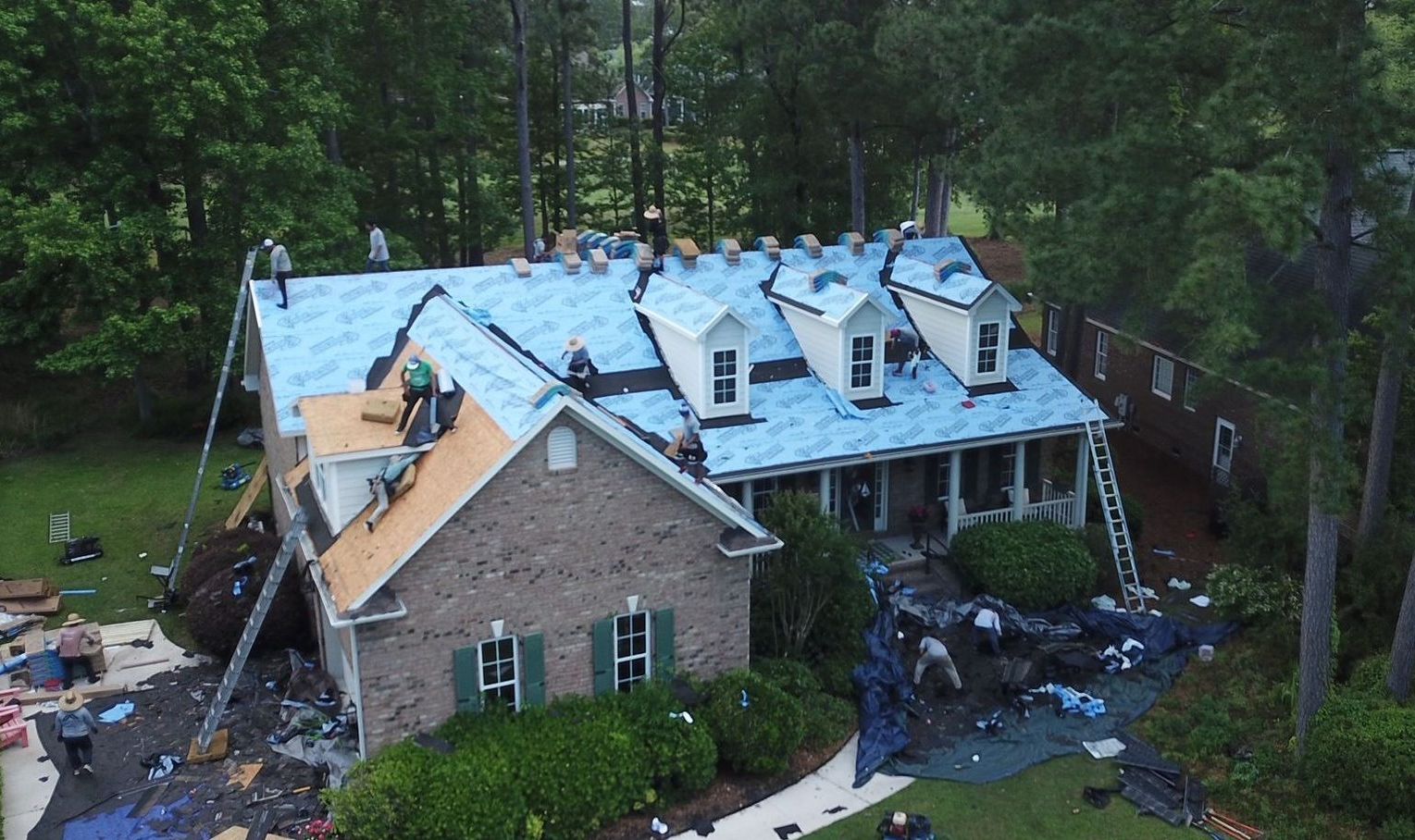 An aerial view of a house being remodeled with a blue roof covering.