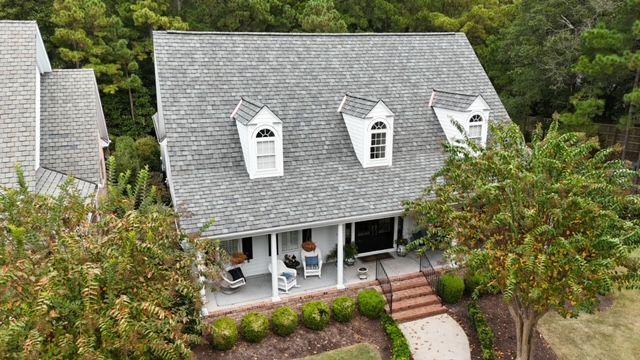An aerial view of a house with a new roof and a large porch surrounded by trees.