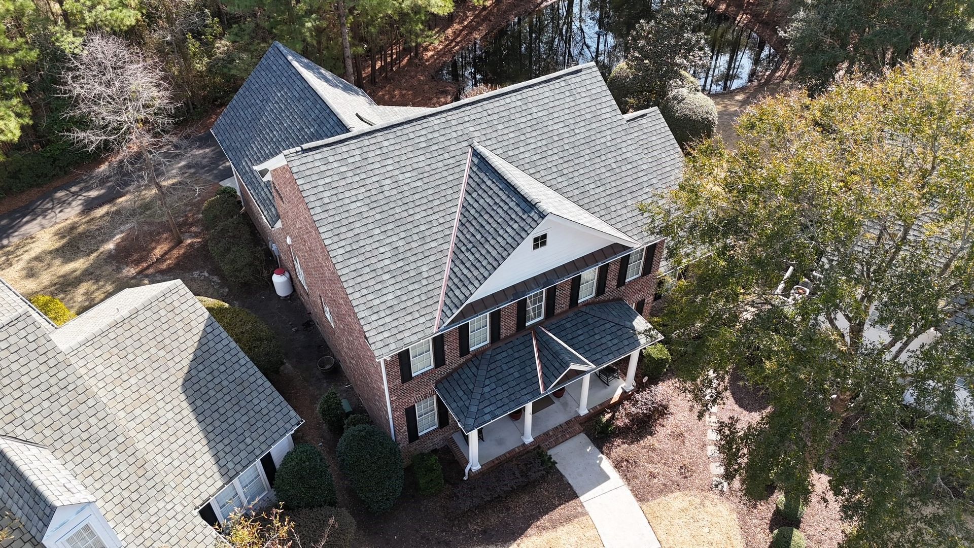 An aerial view of a large brick house with a gray roof surrounded by trees.