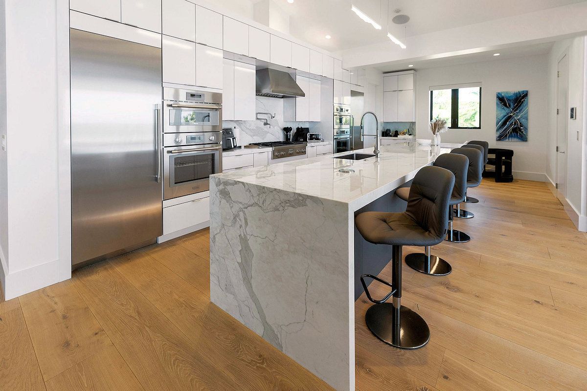 The Oasis, a kitchen with white cabinets and stainless steel appliances and a large island .