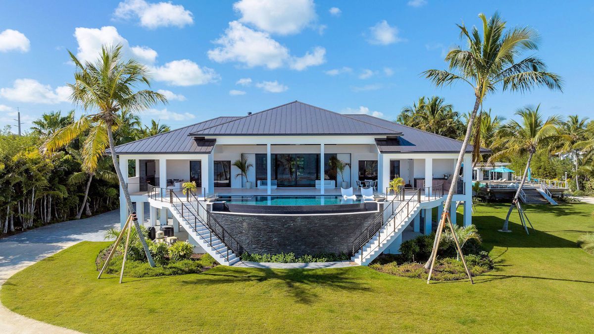 The Oasis, a large house with a swimming pool in the middle of a lush green field surrounded by palm trees .