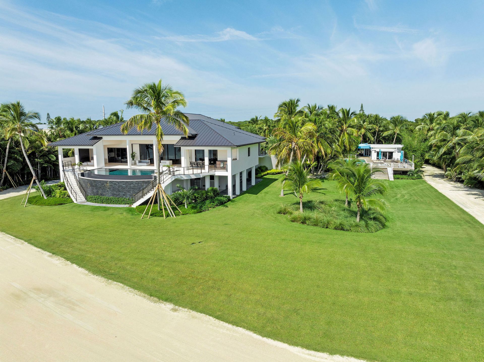 The Oasis, an aerial view of a large house with a pool in the middle of a lush green field .