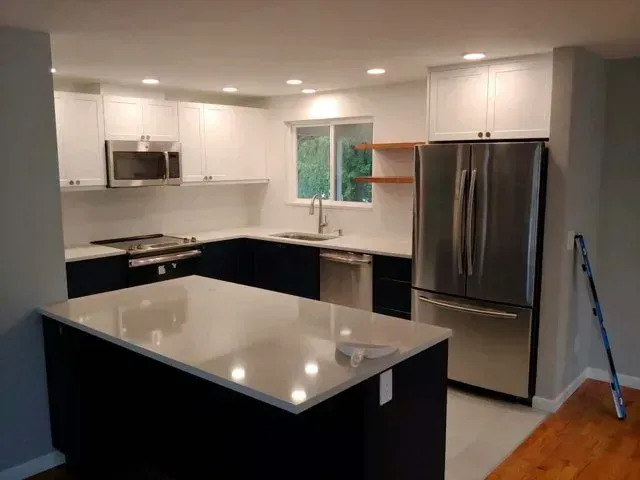 Modern kitchen with white cabinets, dark island, stainless steel fridge, and hardwood floor