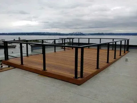 Wooden dock platform with black railings beside calm water under a cloudy sky