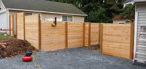 Wooden fence and gate enclosing a gravel driveway beside a house and shed