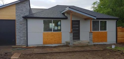 Front view of a small modern house with gray siding, a porch, and unfinished front yard construction.