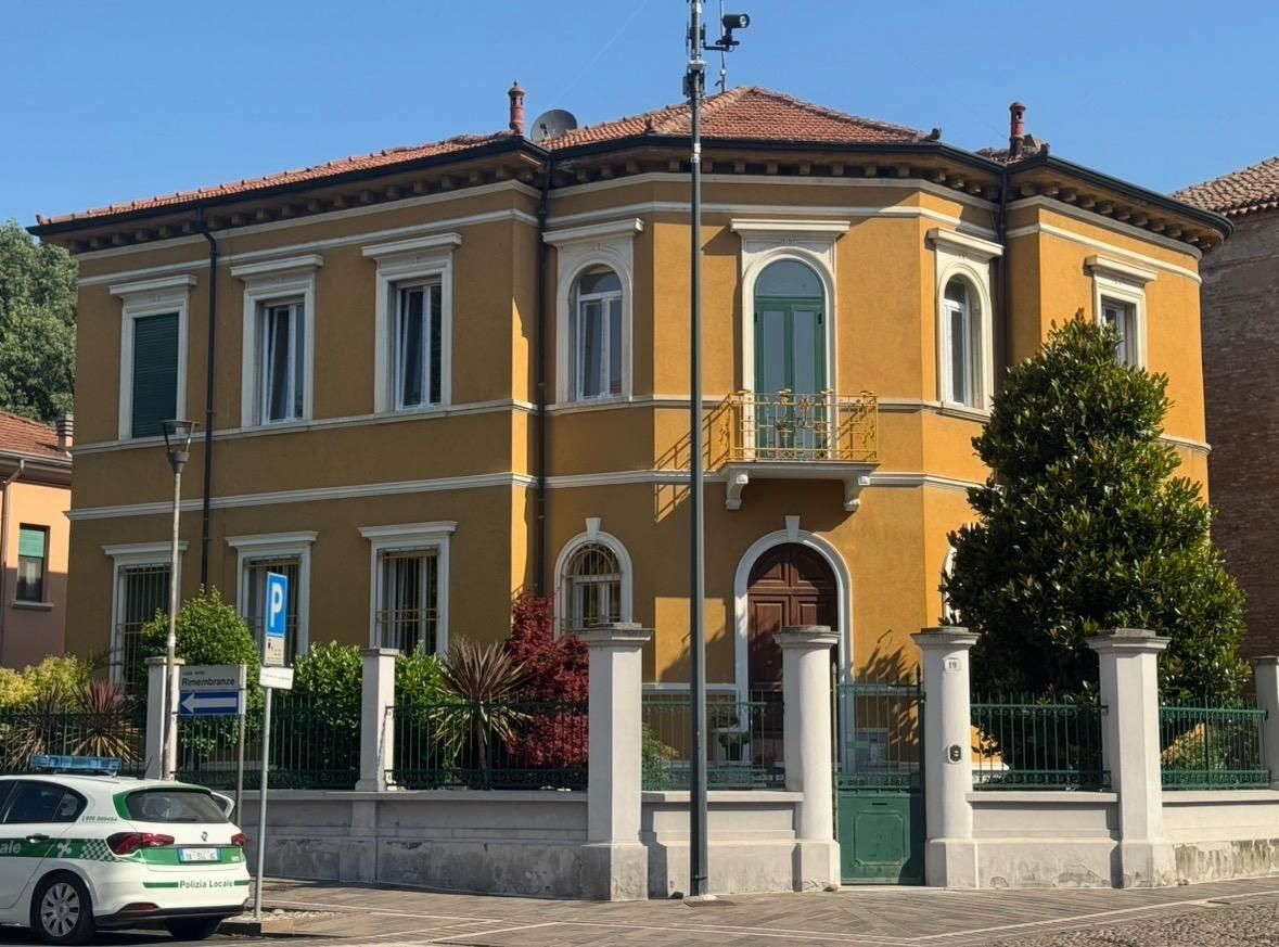 Casa gialla a due piani con tetto di tegole rosse, finiture bianche e recinzione frontale, affacciata su una strada.