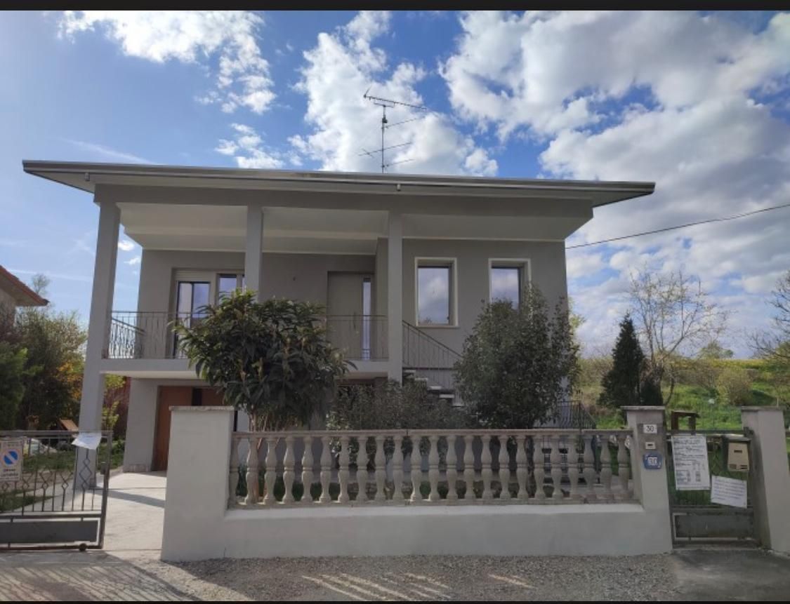 Casa grigia a due piani con recinzione bianca sotto un cielo azzurro nuvoloso