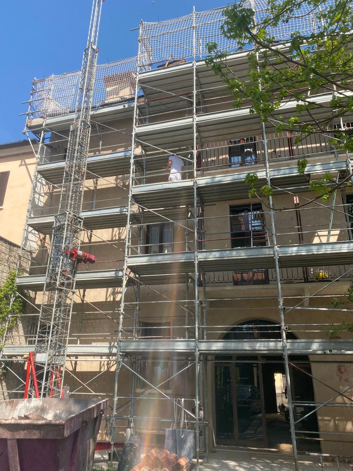 Facciata dell'edificio coperta da impalcature durante i lavori di ristrutturazione sotto un cielo azzurro e limpido.
