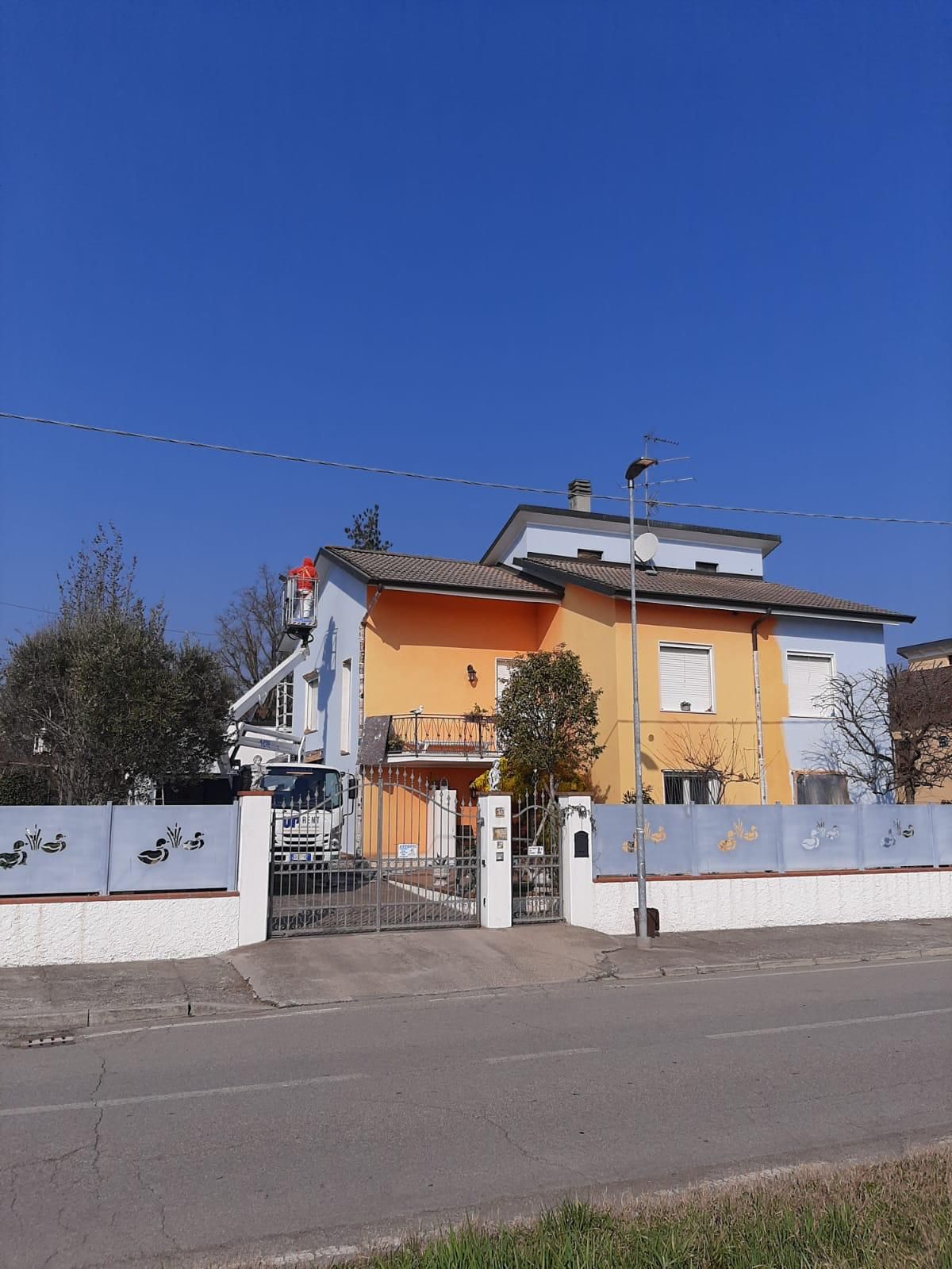 Casa gialla con recinzione e cancello bianchi lungo una strada tranquilla sotto un cielo azzurro limpido.