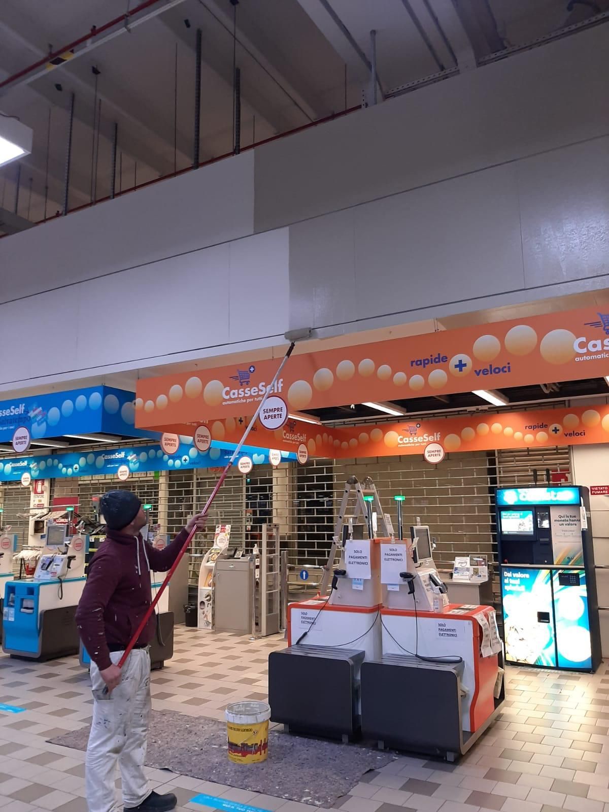 Una persona si trova vicino all'ingresso di un negozio ben illuminato con insegne arancioni e all'interno del centro commerciale si vedono dei carrelli della spesa.