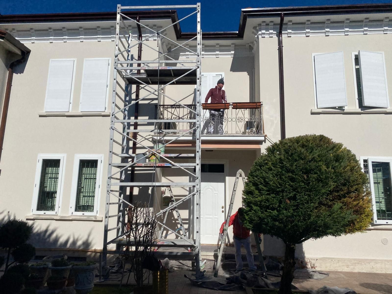 Operaio su un'impalcatura all'esterno di un edificio beige con persiane bianche e un balcone.