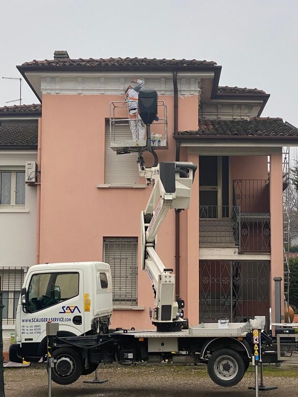Un operaio su una piattaforma aerea ripara la facciata di un edificio color pesca.