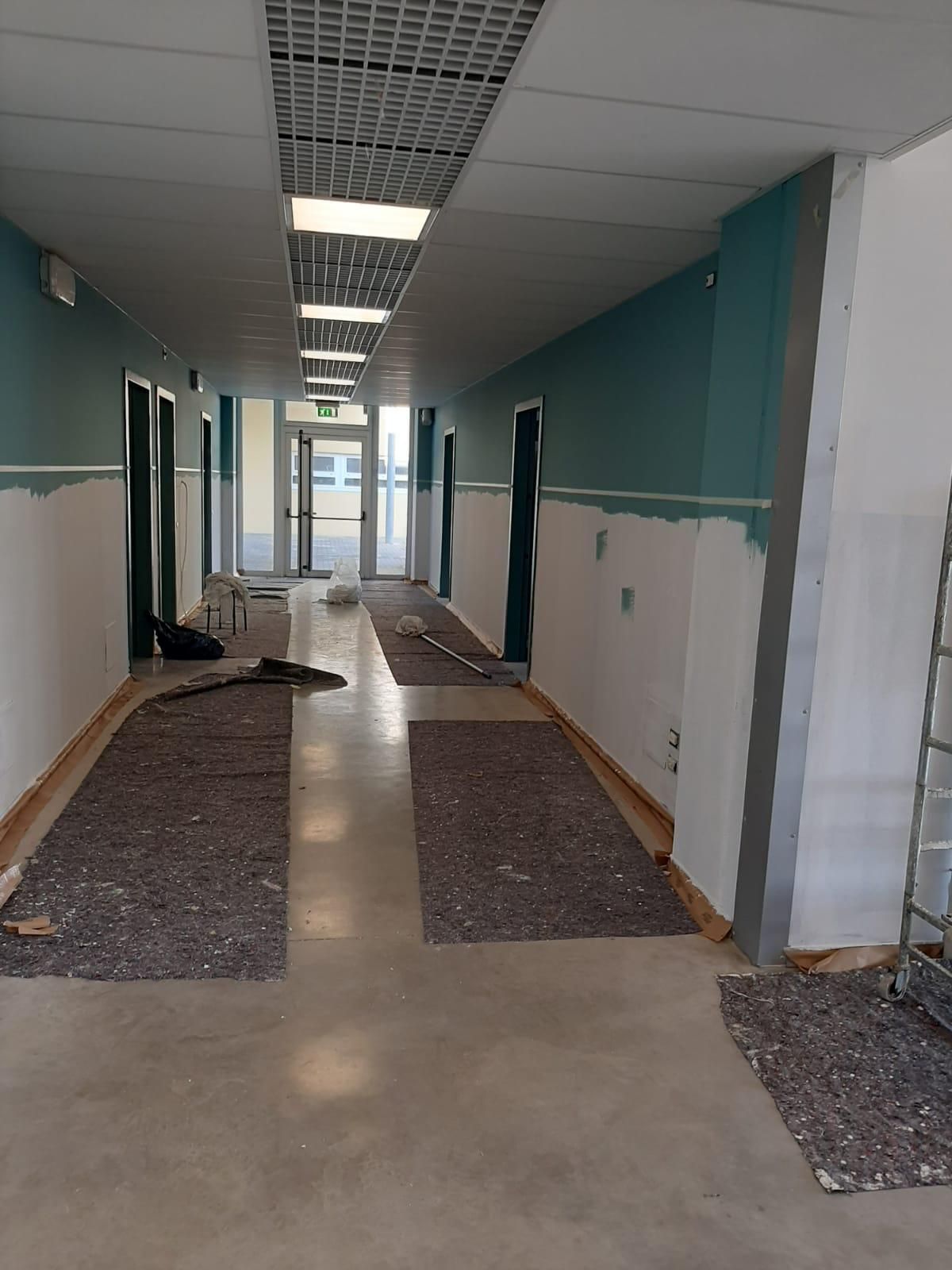 Stretto corridoio in fase di ristrutturazione con pareti a vista, pavimenti e pannelli del soffitto rimossi.