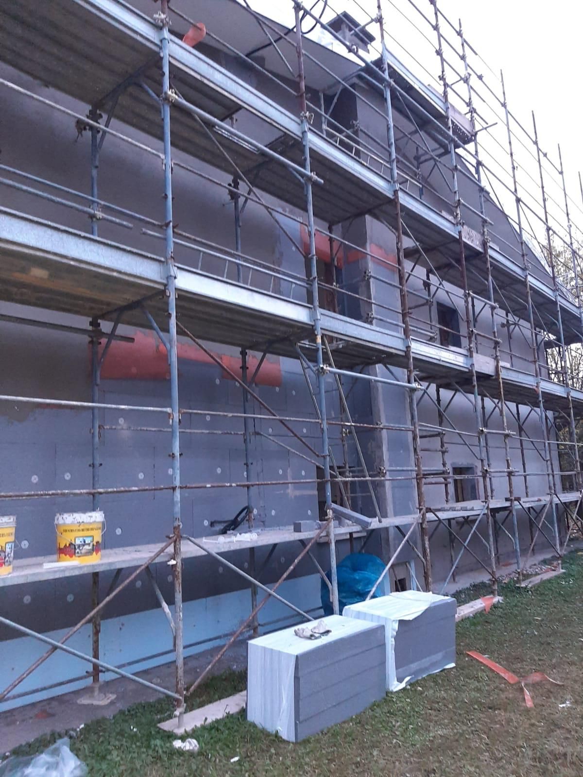 Impalcature attorno a un edificio in costruzione, con scatole di metallo bianche e grigie davanti.