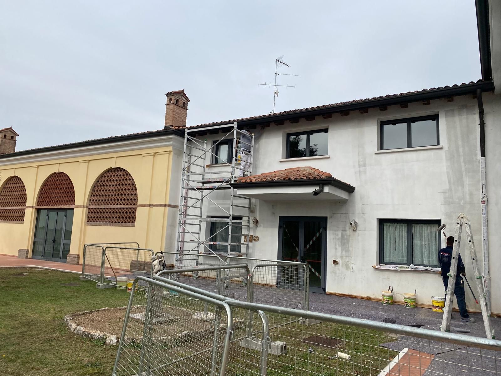 Casa a due piani danneggiata con finestre rotte, impalcature e cortile recintato in fase di riparazione.