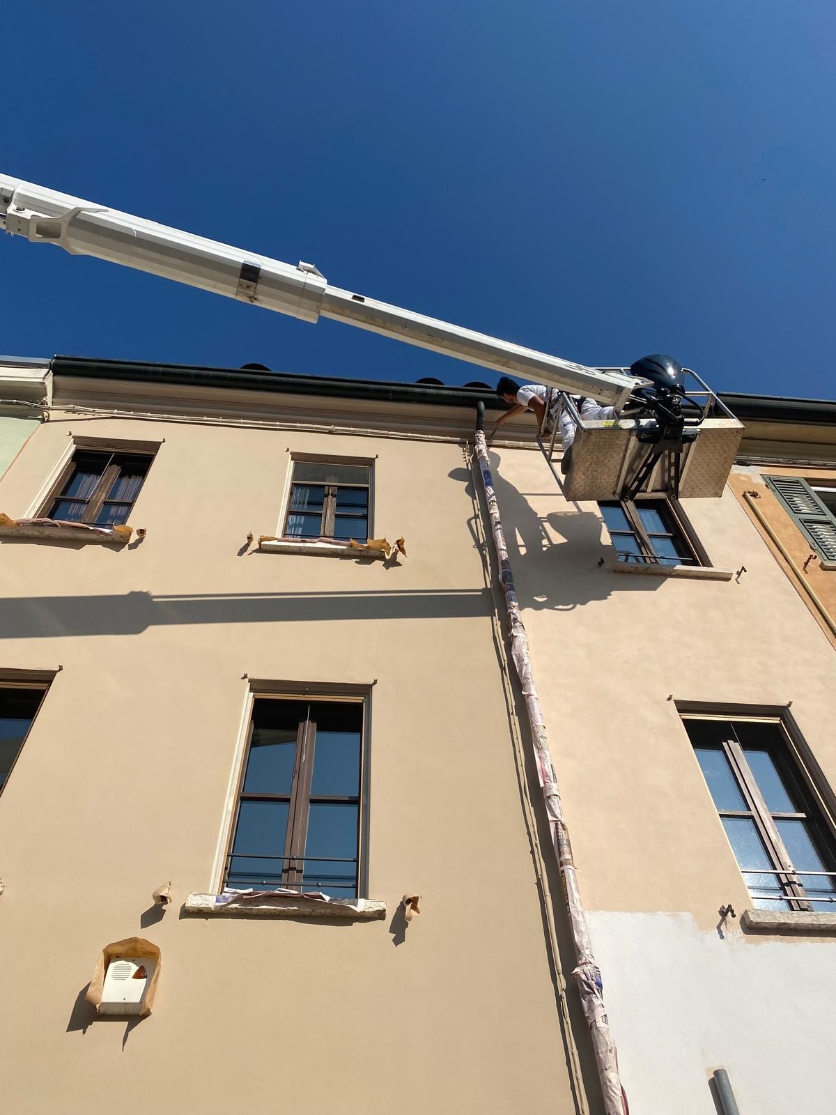 Vista dal basso della facciata di un edificio beige con finestre e del braccio di un camion di servizio soprastante, sullo sfondo di un cielo azzurro.