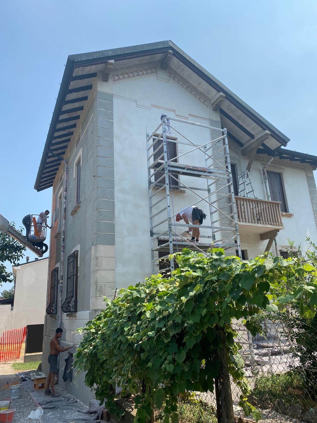 Esterno della casa in costruzione con operai su impalcature e un cespuglio frondoso davanti