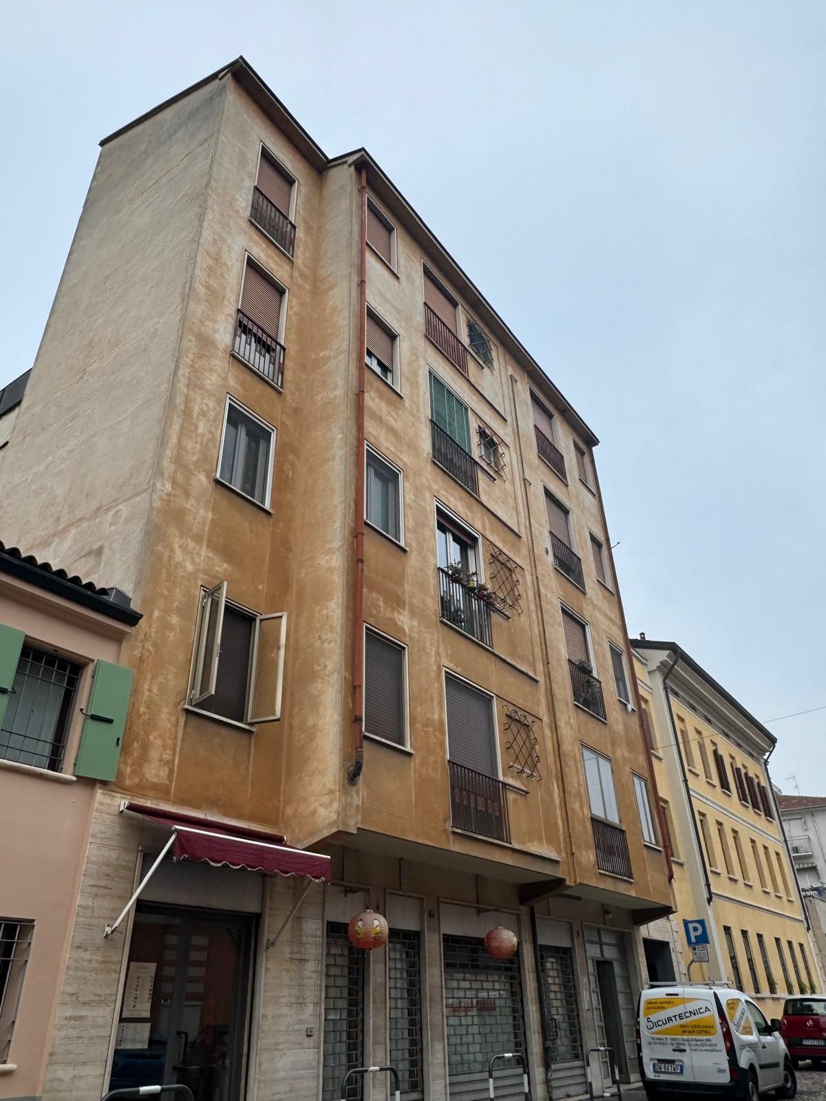 Alto palazzo residenziale dall'aspetto trasandato con negozi al piano terra, situato all'angolo di una strada cittadina.