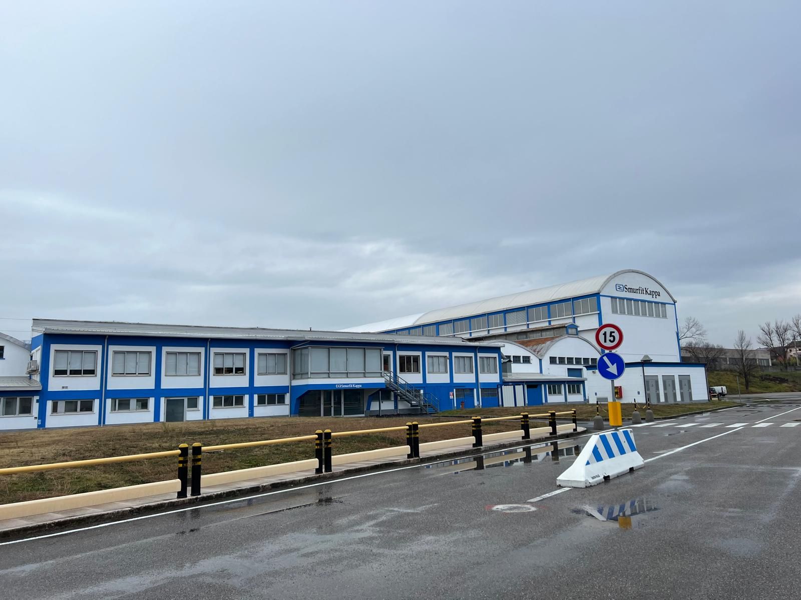 Edificio blu e bianco a bordo strada, con strada bagnata e cielo nuvoloso.