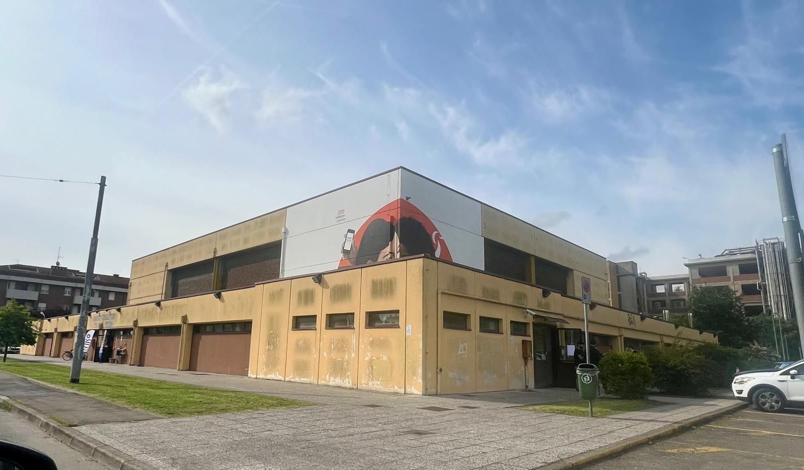 Un edificio angolare a due piani così moderno, con pannelli bianchi e un murale rosso contro un cielo limpido.