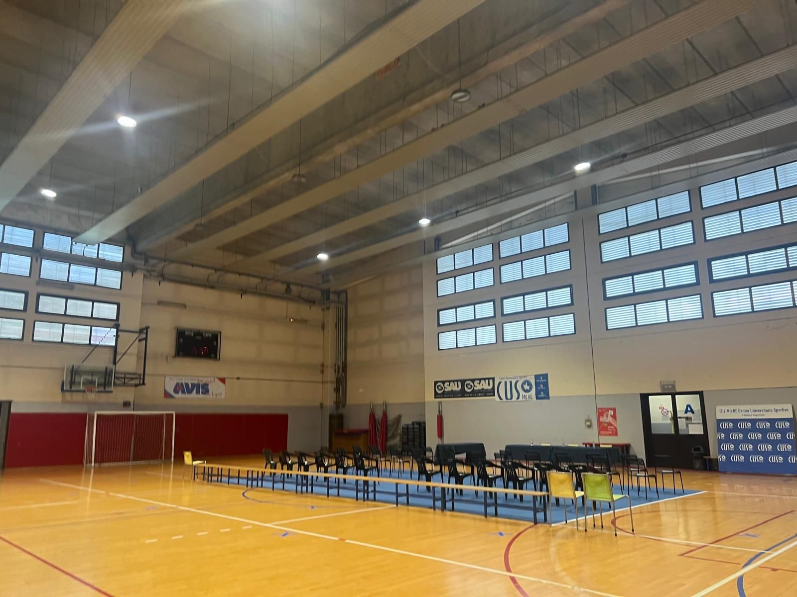 Palestra al coperto con campo blu, lunghi tavoli e sedie allestiti per un evento.