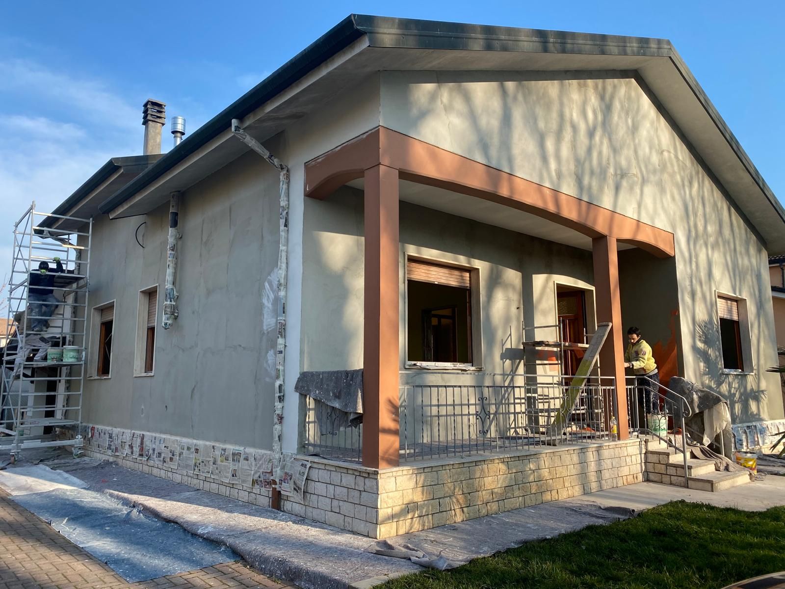 Esterno di una casa di nuova costruzione con stucco beige, finiture arancioni e portico anteriore in fase di costruzione.