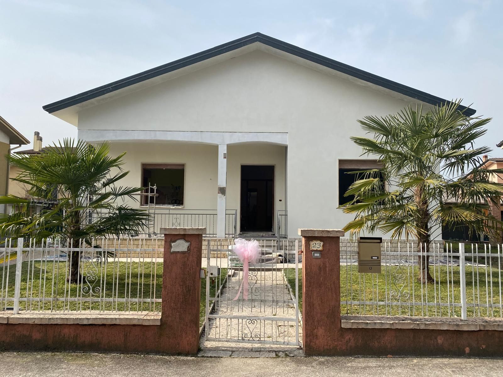Piccola casa bianca con portico anteriore, cortile recintato e vialetto con cancello.