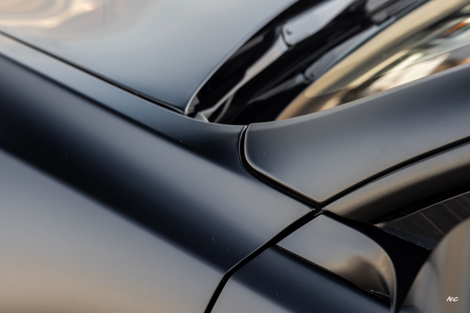 Close-up of a matte black car body, showing the hood, windshield base, and door edge.