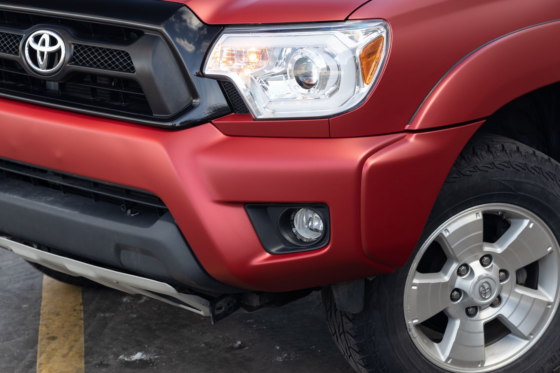 Red Toyota Tacoma truck front detail with headlight, fog light, and wheel.