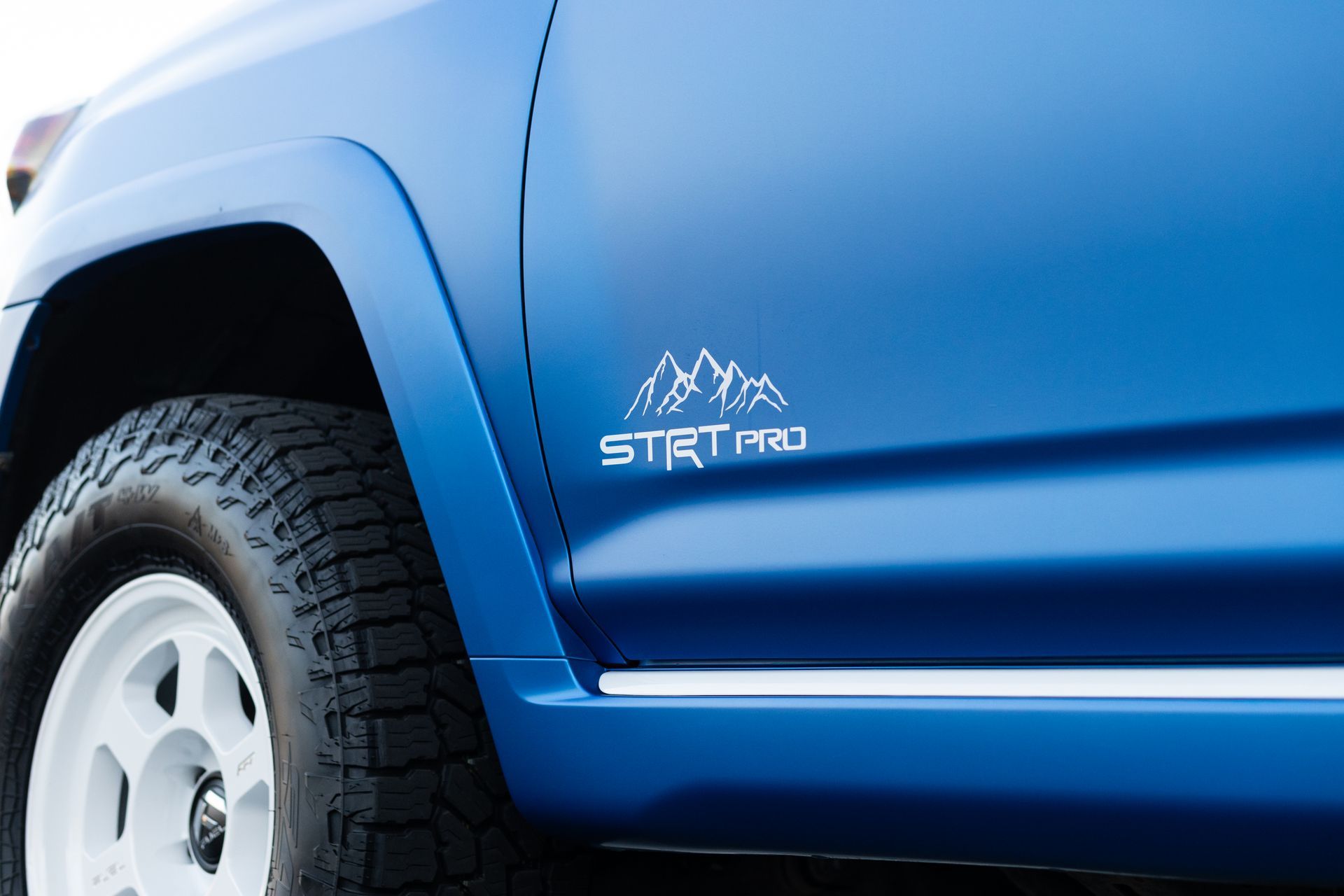 Blue off-road vehicle with white wheels and a mountain logo that says 