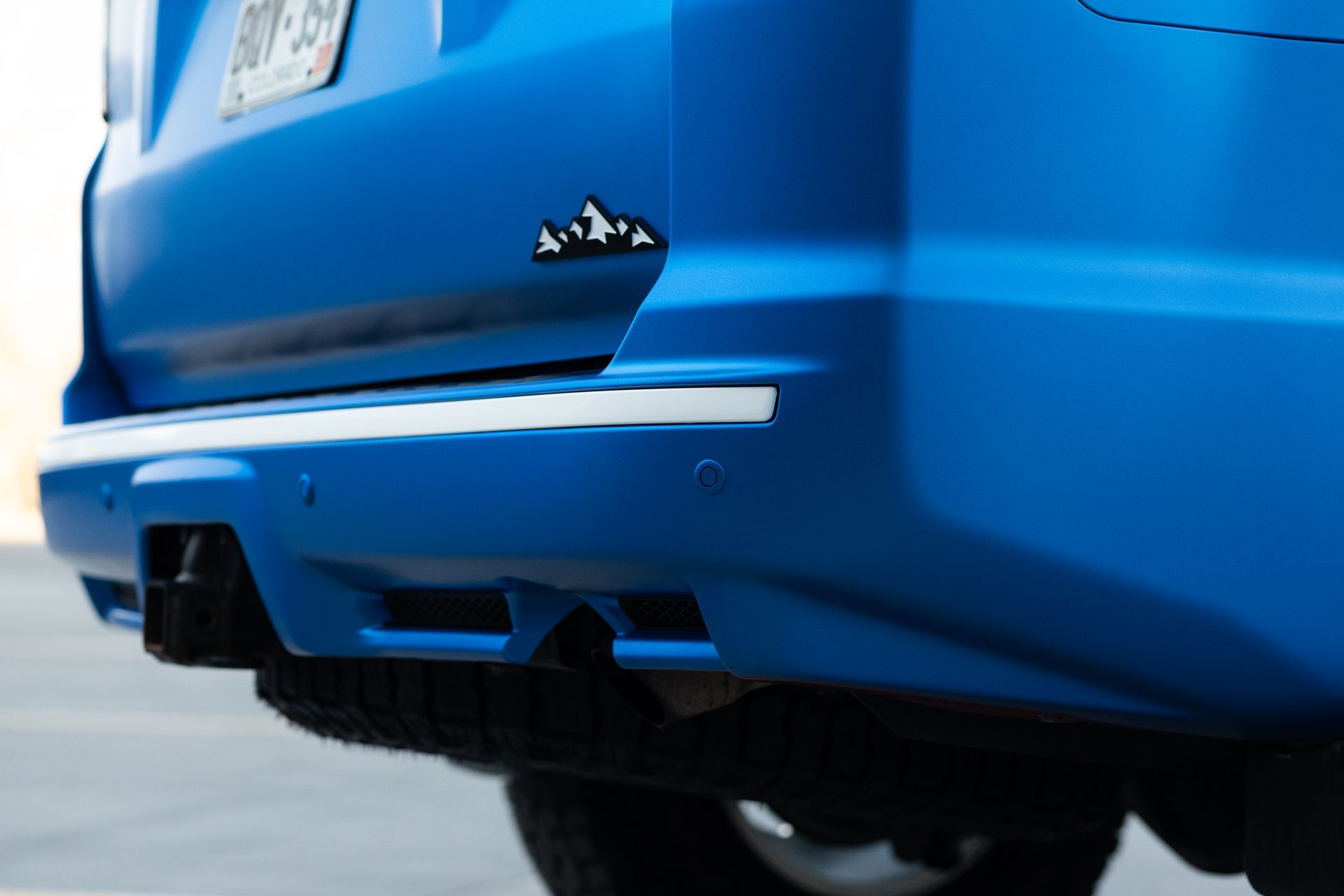 Blue car rear bumper with a mountain emblem and chrome trim.