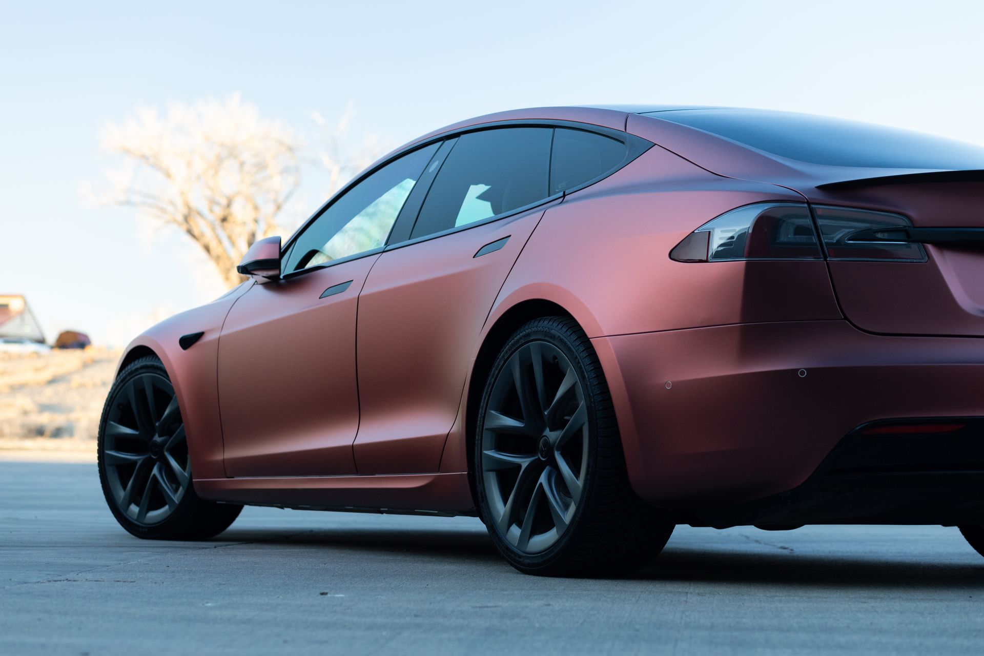 Tesla Model S with matte red-brown finish and black wheels parked outside on a sunny day.