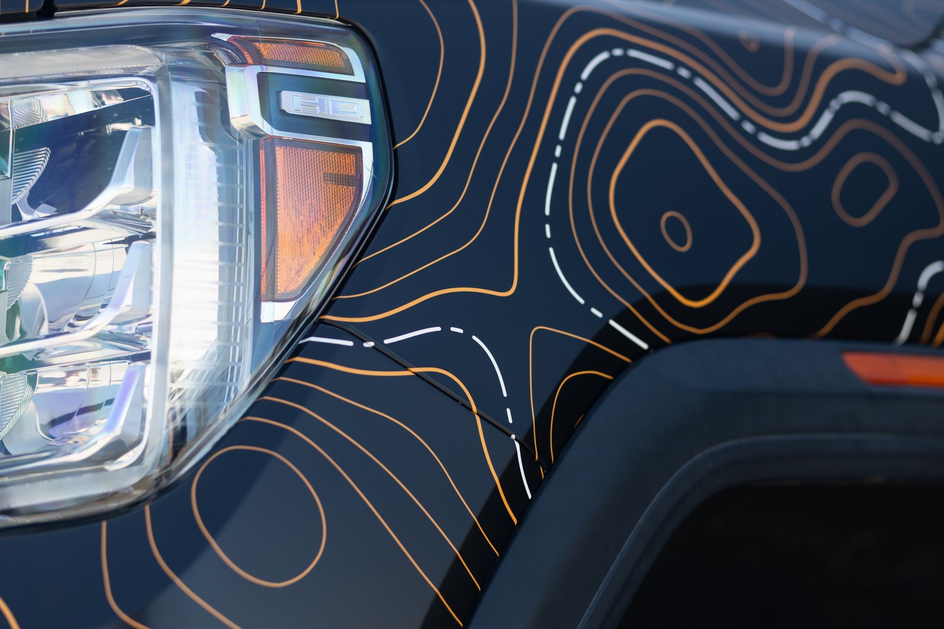 Black car with orange and white topographic map pattern on the hood. Headlight and side marker visible.