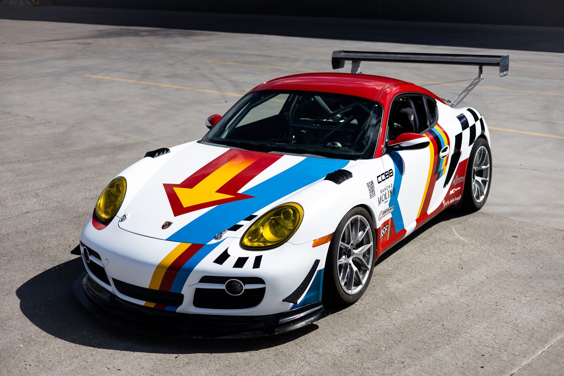 White Porsche race car with colorful stripes, a red roof, and a rear wing on a gray surface.
