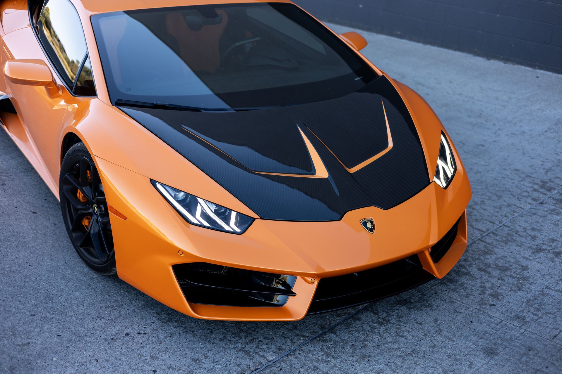Orange Lamborghini with black hood on asphalt.