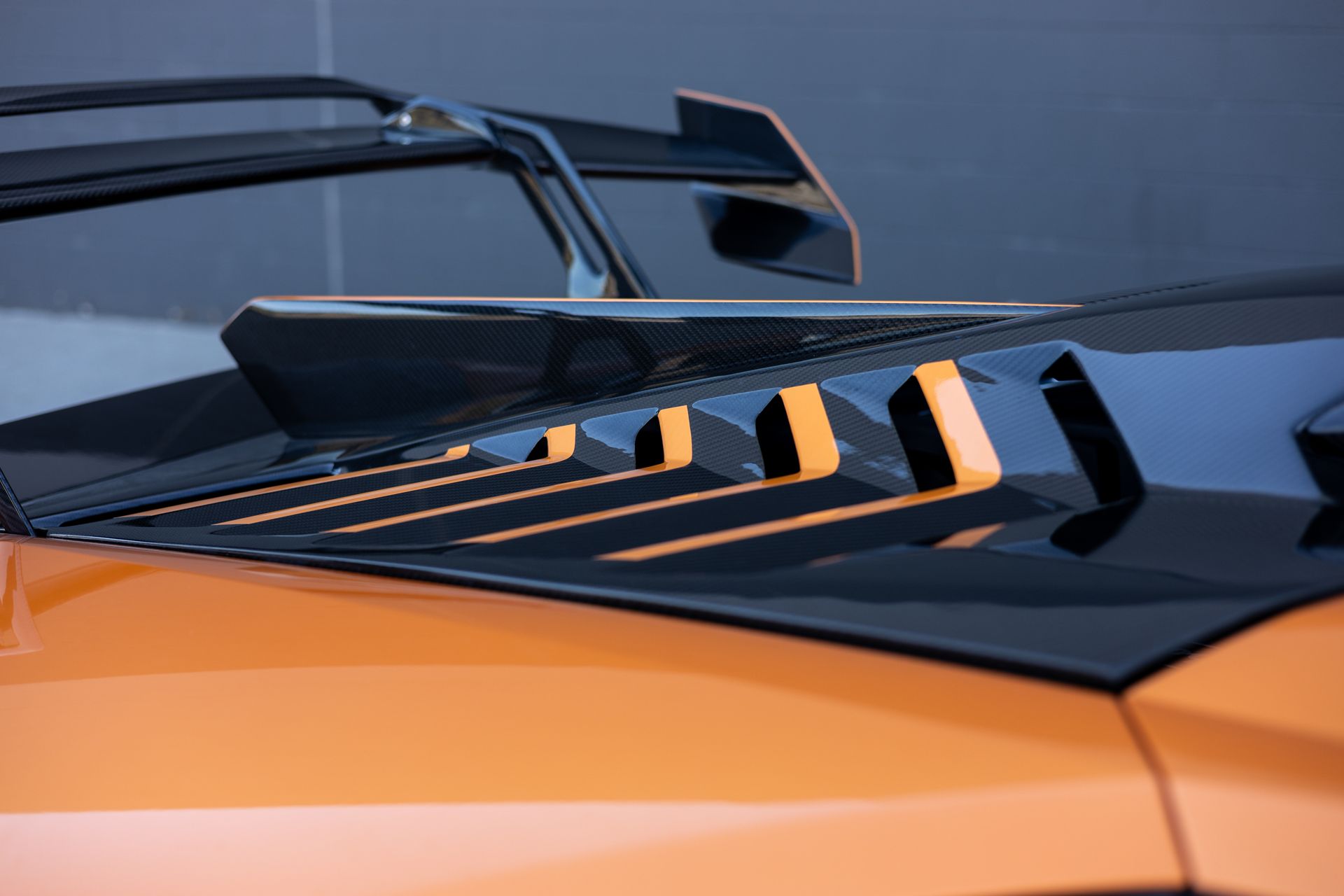 Orange sports car hood with black air vents and spoiler.