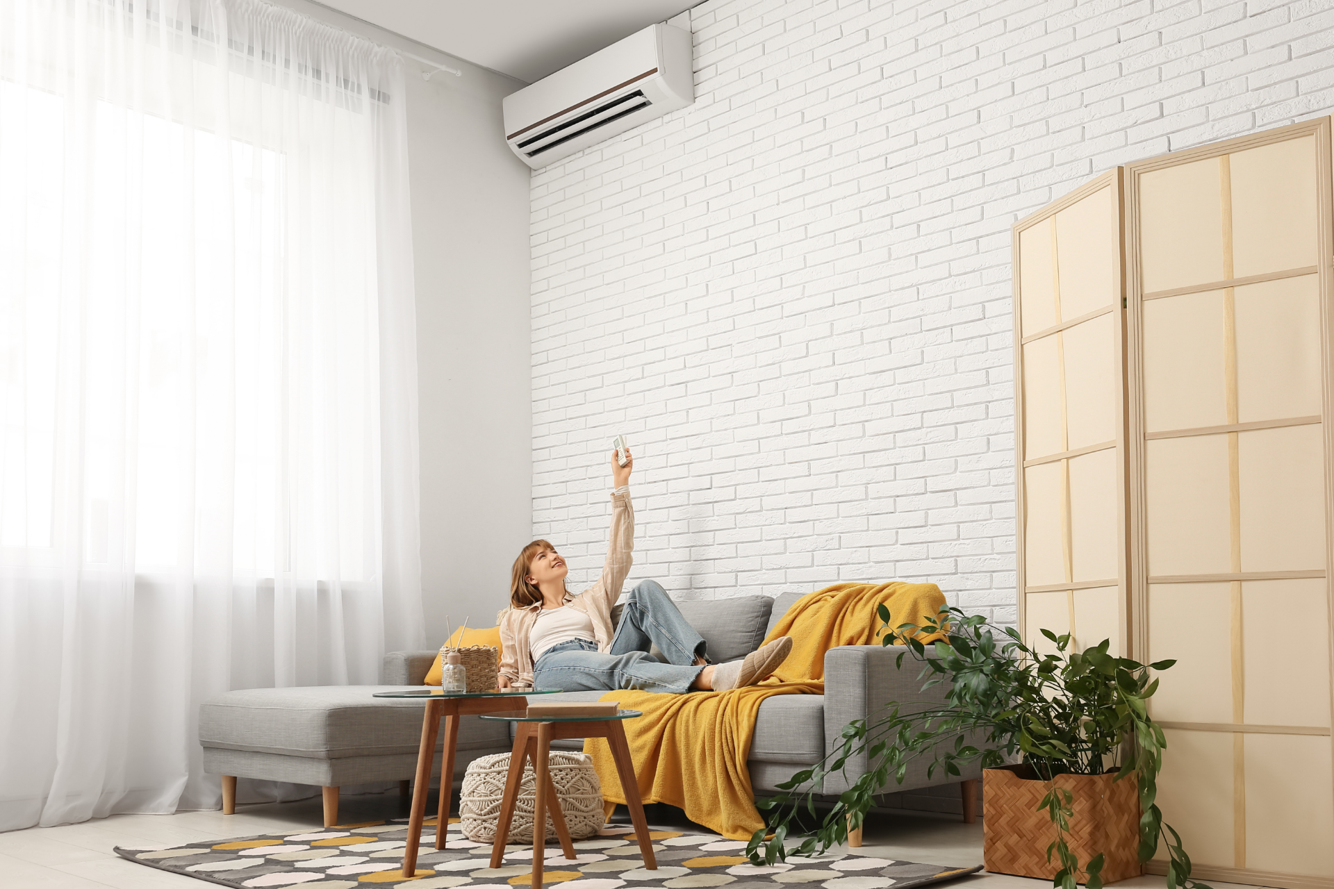 Person relaxing on a sofa in a bright living room, reaching up beside a coffee table and floor plant.