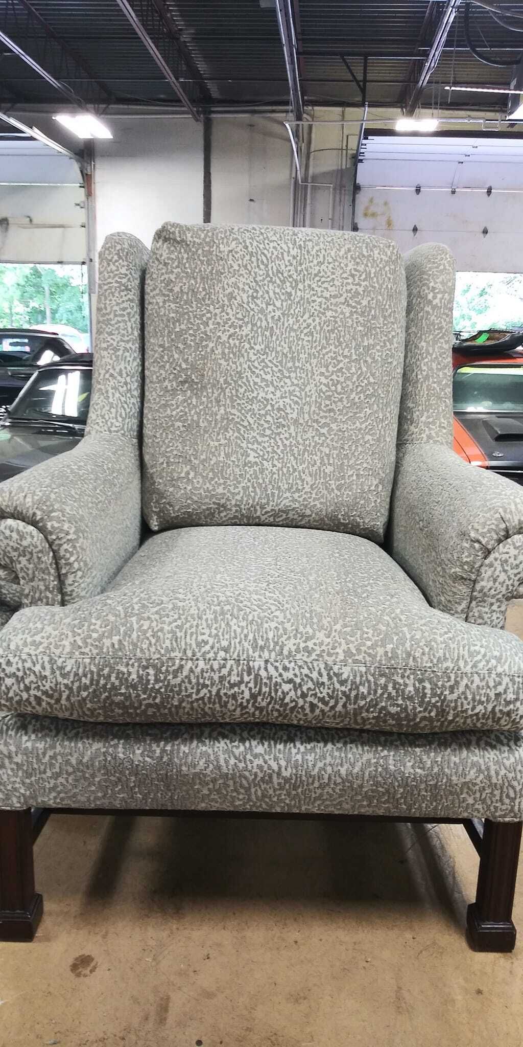 An upholstered wingback chair with a grey and white patterned fabric, set on dark wooden legs in a garage setting.