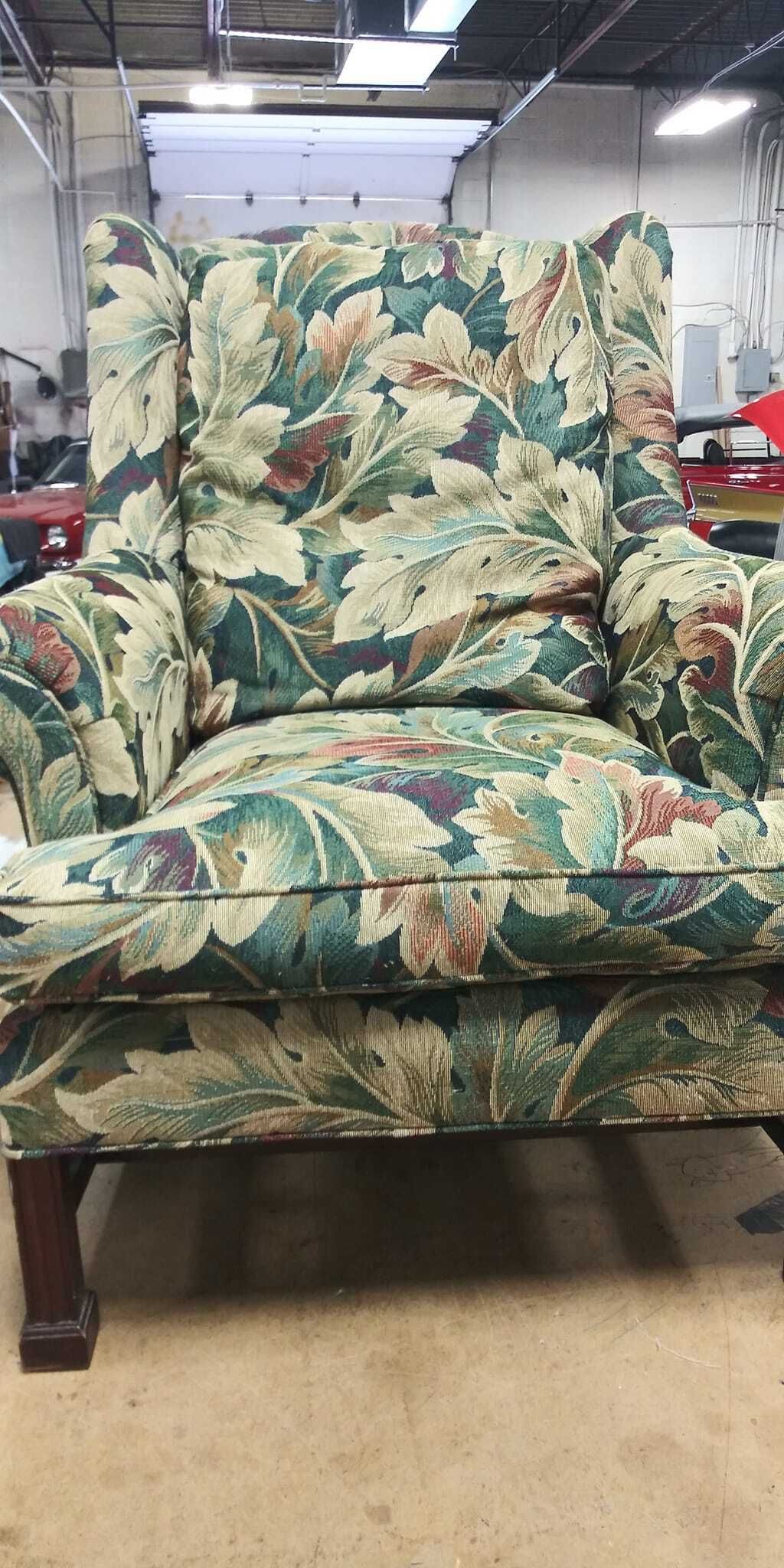 A wingback chair upholstered in a decorative floral fabric with green, cream, and brown tones, set in a workshop space.