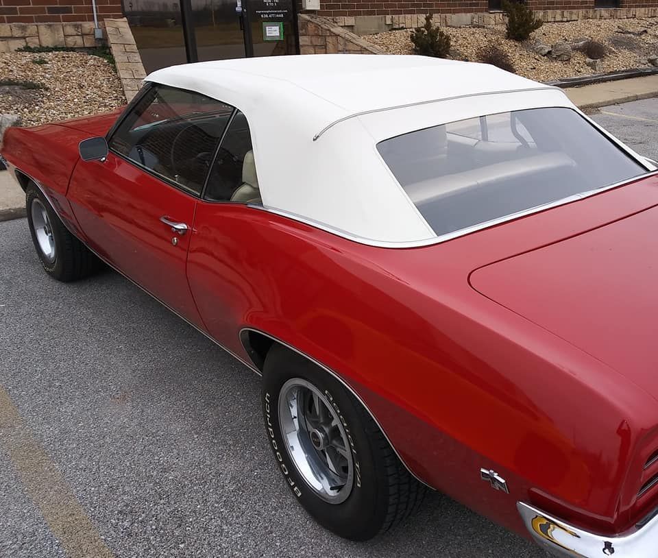 A bright red convertible with a white top and chrome wheels parked in a parking lot.