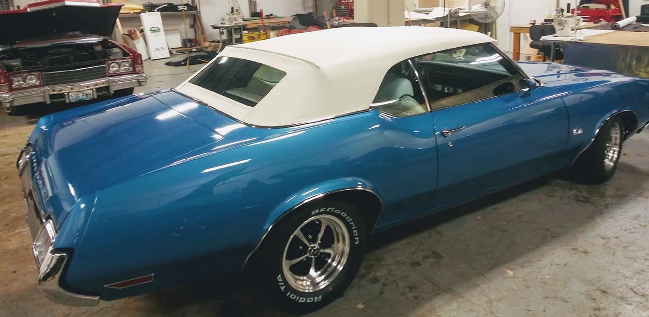 A bright blue convertible car with a white soft top parked inside a garage.