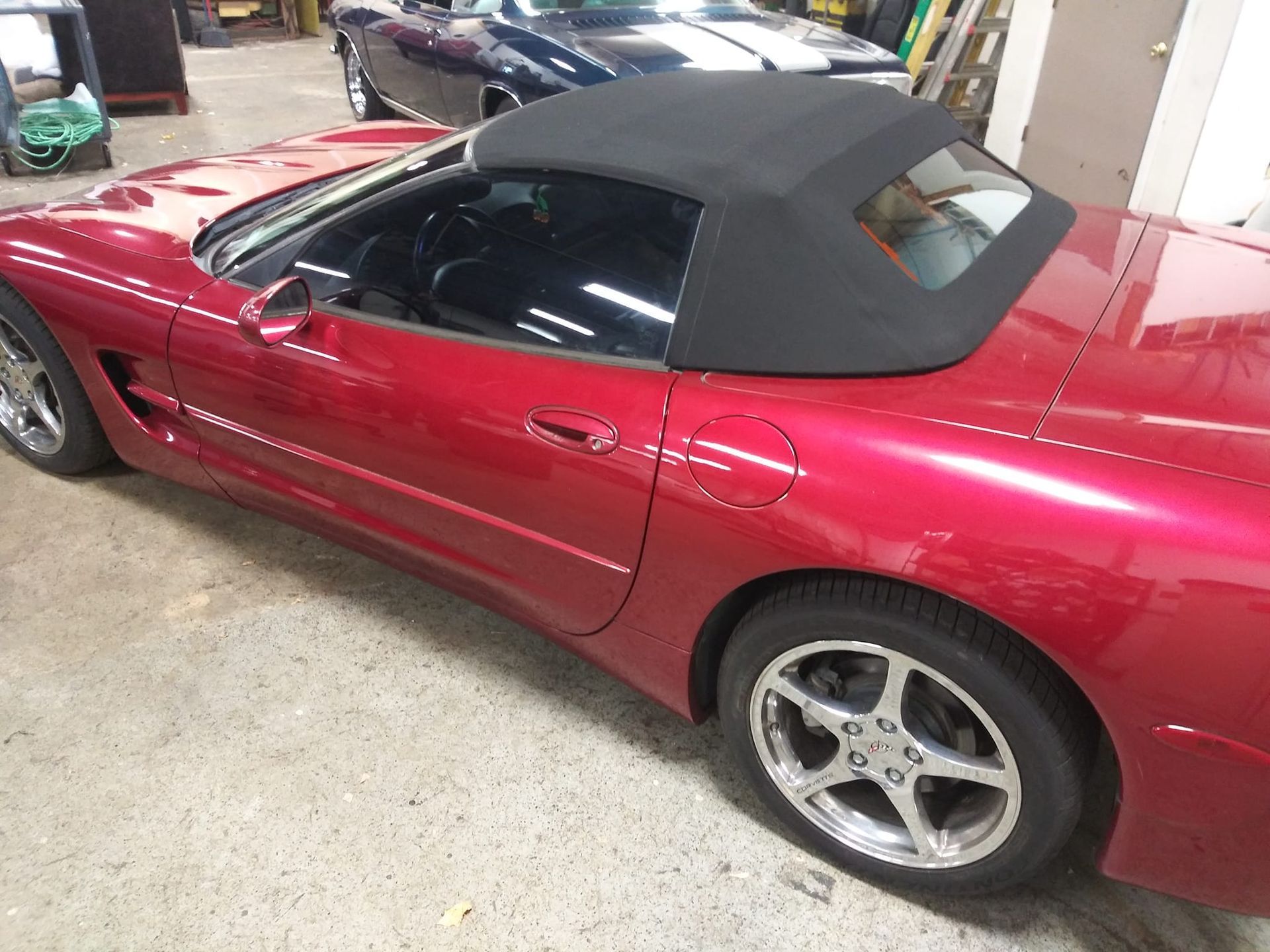 A red convertible Corvette with a black soft top parked in a garage.