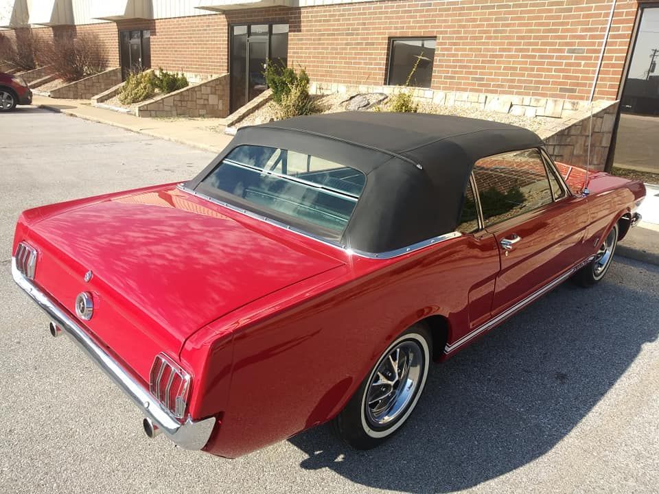 A red vintage Ford Mustang convertible parked in an outdoor lot on a sunny day.