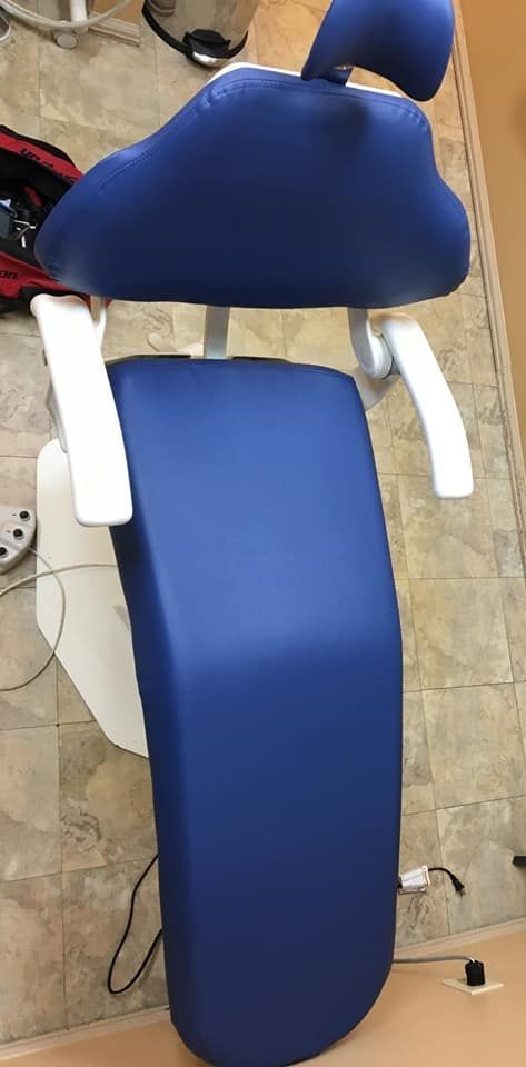 A blue-upholstered dental chair with white armrests, shown from a top-down view on a tiled floor.