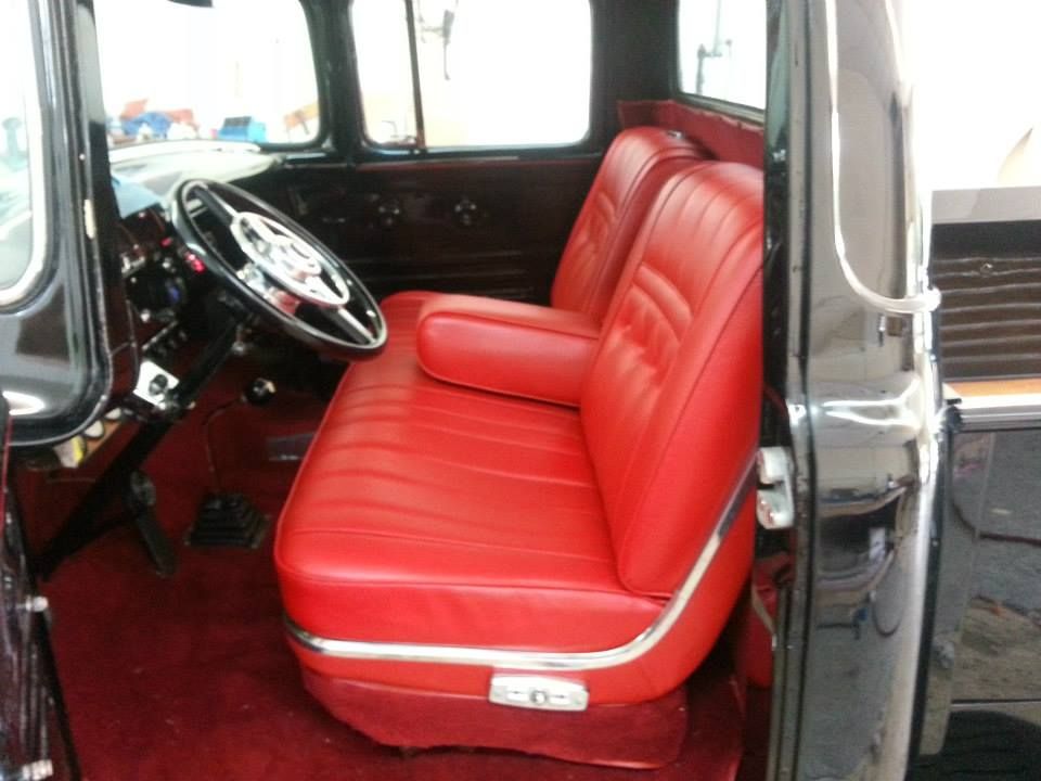 Interior of a black classic truck featuring bright red leather bench seating, a steering wheel, and red carpeting.