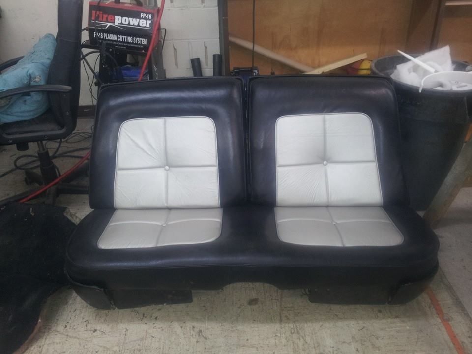 A black and white bench seat with a button-tufted design, positioned in an indoor workshop area.